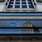 Fachada de edifício comercial com grandes painéis de vidro e a identificação “Banco Master” visível na entrada principal.